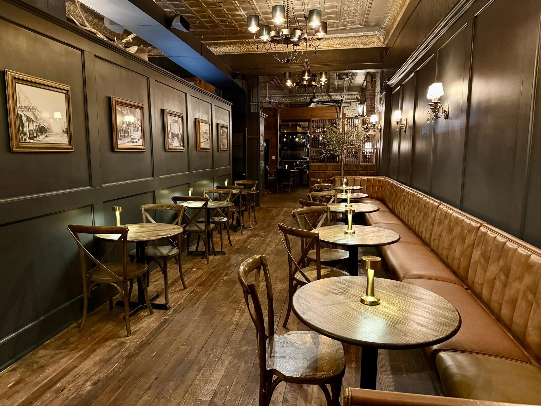 The long room at 221 Social: wood floors, dark wainscoting, chandeliers and leather banquettes